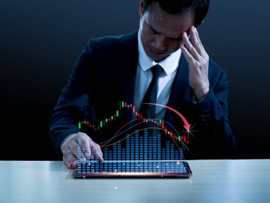 Takım elbiseli Asyalı bir adam masasında oturuyor, sol eli başının üstünde, üzgün bir yüz yaptı. Sağ elini masaya koydu. Ekrandaki tabletin kenarı önemli ölçüde düşen bir hologram gramı gösteriyor..