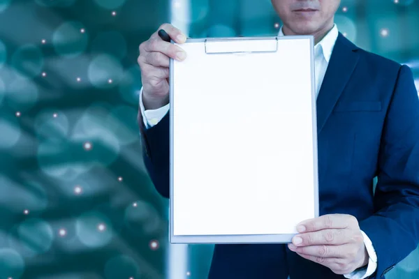 A man in a suit holds an empty file folder(white color)forward. Blurred white and orange lights background