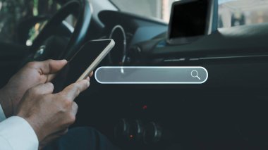 Arabada oturan bir adam mobil bir uygulama kullanarak internet hizmetlerini aramak için cep telefonu kullanıyor. Konsept, mobil bir cihaz vasıtasıyla her yerde bir şeyler bulmanın kolaylığı..