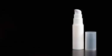 Siyah arka planda izole edilmiş beyaz krem ya da losyon şişesi. Yerde beyaz gölgeler bulanıklaşıyor.