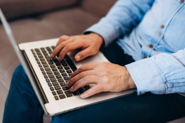 Klavyede yazan erkek ellerini kapat. Orta yaşlı bir adam haber okumak ya da e-postalara cevap vermek için modern dizüstü bilgisayar kullanıyor. Mavi gömlek ve kot pantolon. Modern teknoloji kavramı.