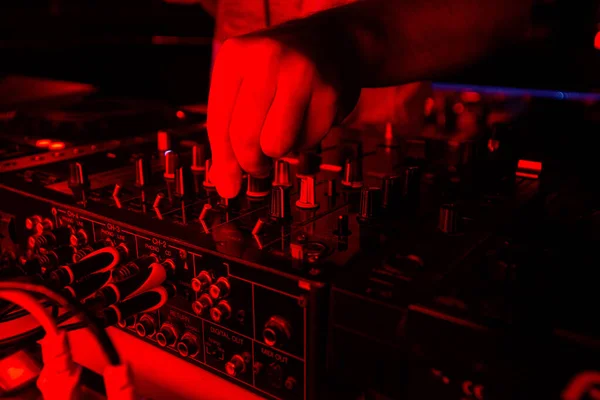 DJ mixer in bright red light. Cut close up shot of male hand turning tumblers on disk jockey console. Nightlife concept. Rave at the party with good music.