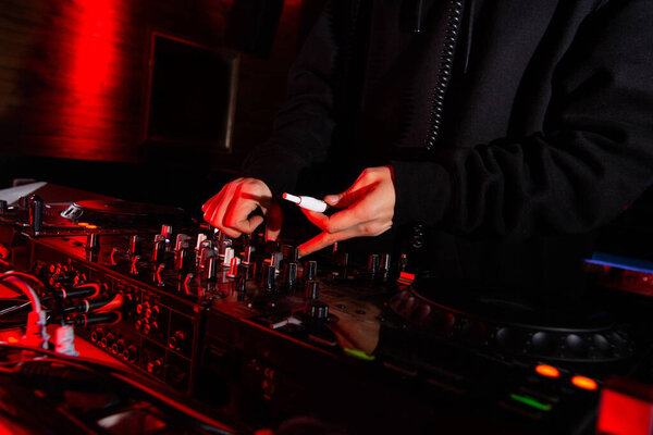 Male DJs hand turn tumblers and hold electronic cigarette. Close up shot. Nightlife concept. Man playing music at party in nightclub. Dark atmosphere.