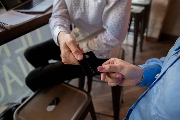 Young man wants to pay off. Close up of mans and womans hands holding credit cart. Cafe or restaurant on background. The freelancer is done with his remote work and wants to pay for the food.