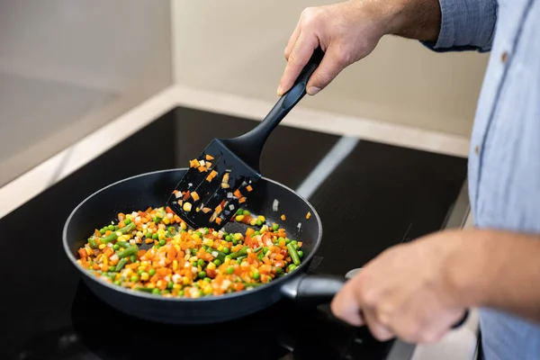 Tencerede güveç renkli sebzeler. Yetişkin adamlar spatula ve karıştırma tabağı tutuyor. Sağlıklı gıda konsepti. Modern mutfak aletleri. Sağlıklı ve lezzetli bir kahvaltı..