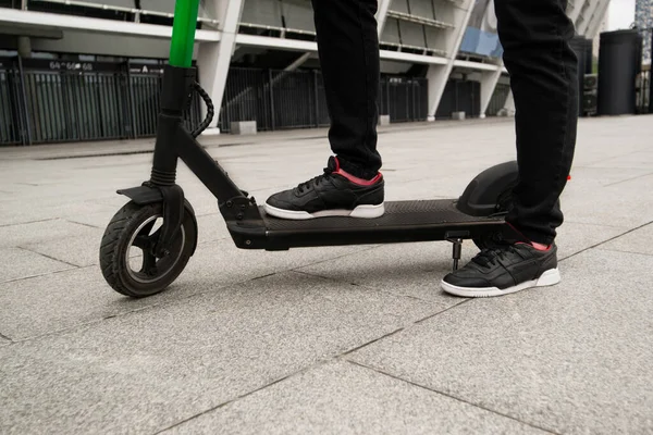 Knip het zicht van mannelijke benen staande op e-scooter. Slimme manier om door een grote stad te rijden. Zwarte stijlvolle sneakers. Hij huurde een elektrische scooter via smartphone applicatie. Eco-gewoonten. — Stockfoto