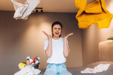 Çaresiz bir kadın dağınık bir odada kanepede oturuyor ve yorgun temizlik ve çamaşırlardan dolayı bağırıyor ve giysilerini öğütüyor. Rutin.