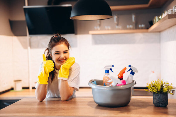 Young happy cute woman in yellow gloves is cleaning her kitchen at home with detergents.