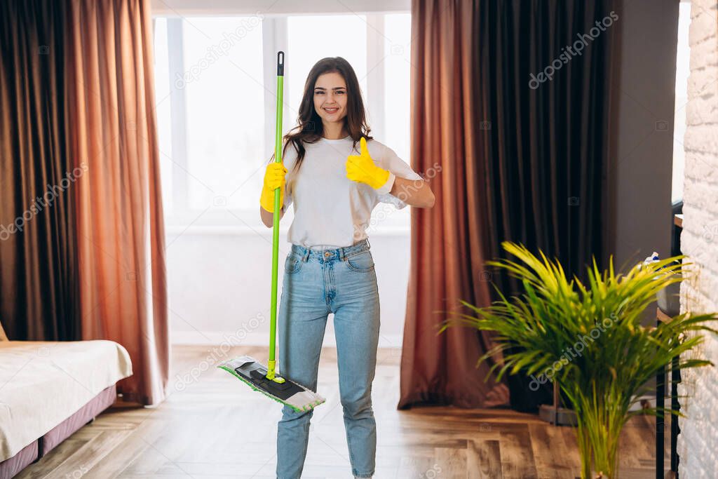 Full length photo of positive cheerful housewife wearing yellow rubber gloves, enjoy washing floor hold mop feel content wearing denim jeans casual clothing in house indoors