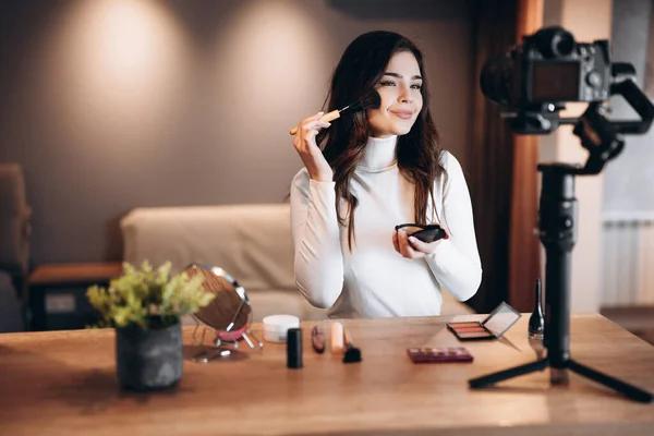 Güzellik blogcusu, güzel bayan günlük makyaj rutin dersini kamerayla çekiyor. Etkilenen genç kadın canlı yayın kozmetik ürünleri eleştirisi ev stüdyosunda. Vlogger işi. DIY makyaj yapıyor