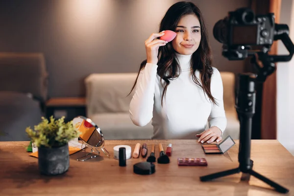 Beauty blogger nice female filming daily make-up routine tutorial on camera. Influencer young woman live streaming cosmetics product review in home studio. Vlogger job. DIY putting makeup