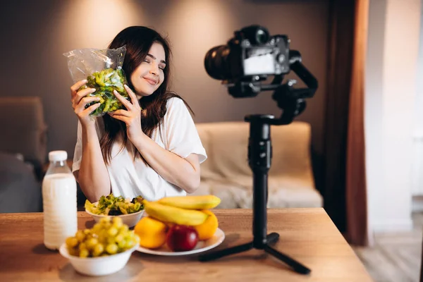 Healthy food blogger young female cooking fresh of fruits vegan salad in kitchen studio, filming tutorial on camera for video channel. Young female influencer shows her love to healthy eating.