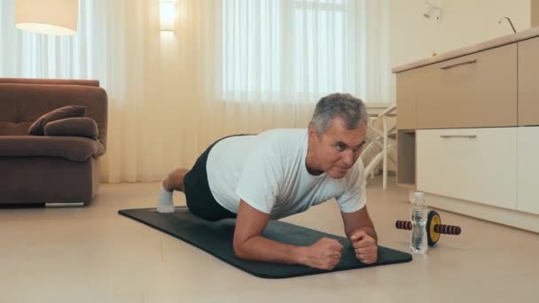 Elderly, mature man doing side plank exercise with raised hand, smiling and looking at camera. Healthy lifestyle concept. Take care of your body. Old sportsman training at home during quarantine. — Stock Video