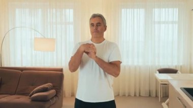 Yaşlı adam elini ısıtmaya çalışıyor. Formda vücut ısıtması olan son sınıf erkek sporcu, evde antrenman yapıyor. Kendine çok iyi bak. Arka planda modern ışık odası. Yaşlı spor konsepti Yakınlaştır