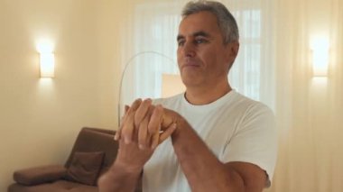Yaşlı adam elini ısıtmaya çalışıyor. Formda vücut ısıtması olan son sınıf erkek sporcu, evde antrenman yapıyor. Kendine çok iyi bak. Arka planda modern ışık odası. Yaşlı spor konsepti Yakınlaştır