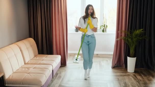 Genç kadın evde temizlik yapıyor. Esmer kadın manken evi temizlerken dans ediyor ve şarkı söylüyor.. — Stok video