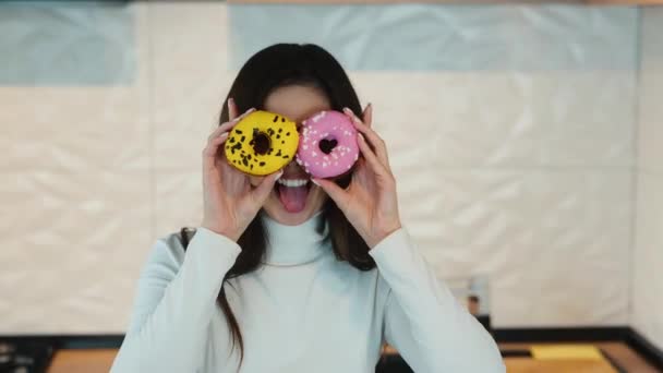 Mujer joven tiene muecas y haciendo caras con rosquillas en la cocina durante el desayuno — Vídeos de Stock