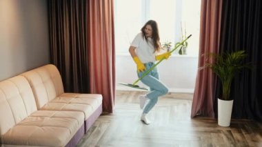 Yavaş çekim. Genç kadın evde temizlik yapıyor. Esmer kadın manken evi temizlerken dans ediyor ve şarkı söylüyor.