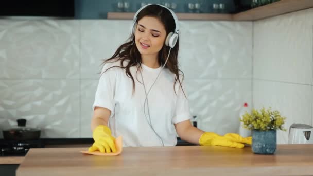Молодая женщина убирает дома. Брюнетка-модель очищает кухонную поверхность на кухне. Девушка слушает музыку и убирает грязь в квартире. Замедленная съемка. замедленное движение. — стоковое видео