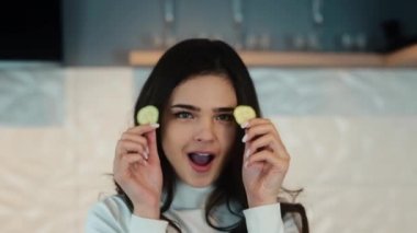 Genç bir kadın mutfak yüzeyinde yemek pişirirken yüzünü salatalık dilimleriyle buruşturuyor. Yanında salatalık, domates, biber, yumurta ve marul yaprakları var. Yavaş çekim görüntüleri