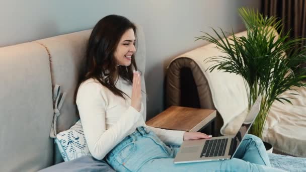 Egy fiatal nő ül a kanapén, okostelefont és laptopot használ. A női modell telefonon beszél, miközben szörfözik az interneten. Technológia, amely az emberek által támogatott kommunikáció. Lassú. — Stock videók