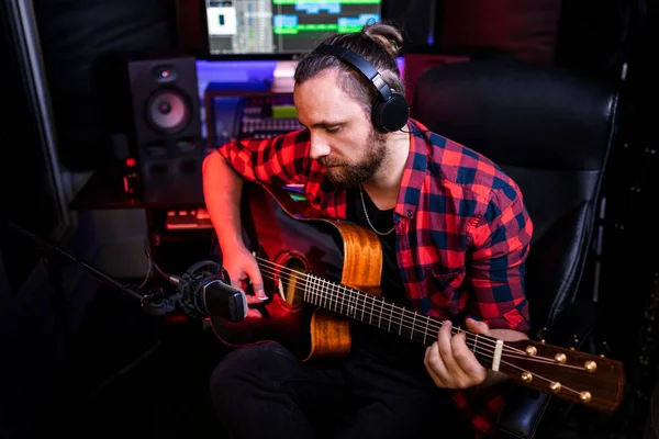 Hipster uomo con la barba in cuffia sta suonando la chitarra e peccando la sua nuova canzone in studio stereo per registrare brano nuovo di zecca — Foto Stock