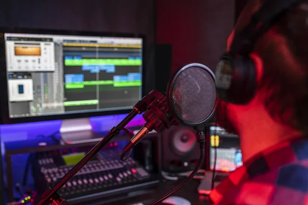 Weißer junger Mann singt und nimmt im Stereo-Studio mit Mischpult und Mikrofon einen neuen Song auf — Stockfoto