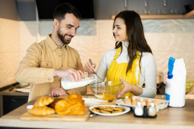 Çiftler yemek pişirirken eğleniyorlar ve birlikte mutlular. Kurabiye ve çörek pişiriyorlar.