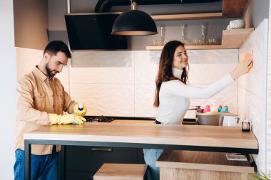 Plastik eldivenli koca ile mutfağı temizleyen çekici bir kız. Temiz bir ev mutlu bir evdir. Modern mutfaklarında günlük kıyafetlerini silen mutlu bir çift. Evi temizleme.
