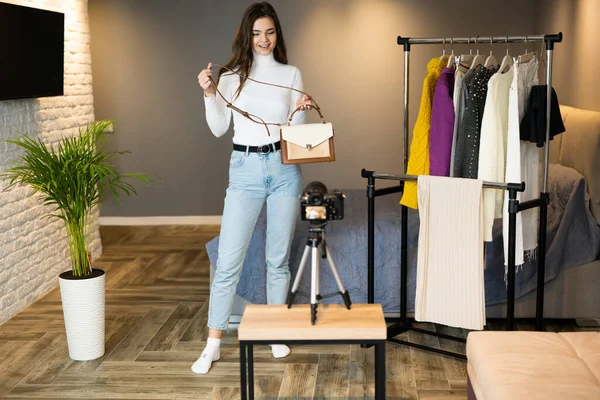 Joven blogger chica con cabello oscuro está mostrando su ropa y bolsas para sus seguidores en las redes sociales para venderla en línea — Foto de Stock