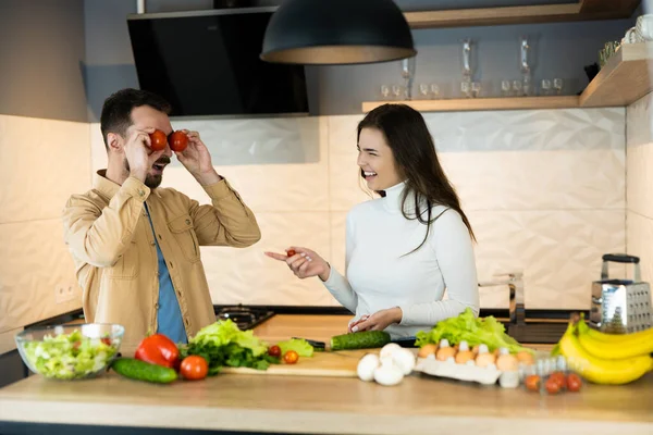 Linda pareja sonríe y se divierte en la cocina. La gente vegana feliz está cocinando ensalada usando solo nutrición y comida saludable — Foto de Stock