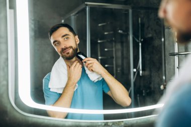 Havluyla aynaya bakan ve sabah erkenden tıraş olan genç yakışıklı bir adam..