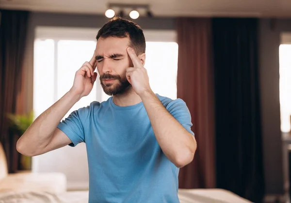Hombre con barba sentado en la cama en casa sufriendo de dolor de cabeza o resaca. Concepto de hora de dormir y descanso — Foto de Stock