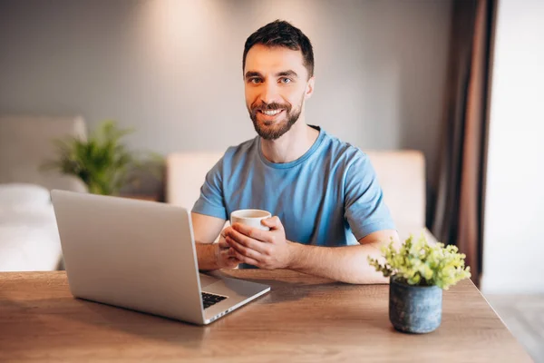 Genç bir adamın elinde bir fincan kahveyle dizüstü bilgisayar kullanarak mutfakta geçirdiği günlük hayat. Evden çalışan çekici bir erkek, uzaktan internet bağlantısı kullanarak evden işe gidiyor..