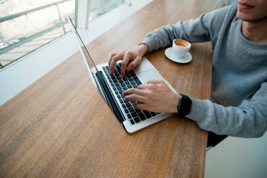 Dizüstü bilgisayarın klavyesindeki erkek eller. Serbest meslek kavramı. Programcı konsepti. Pencerenin yanındaki bilgisayarda çalışan genç adamın önünde bir fincan espresso içerken görüntüsünü kes..