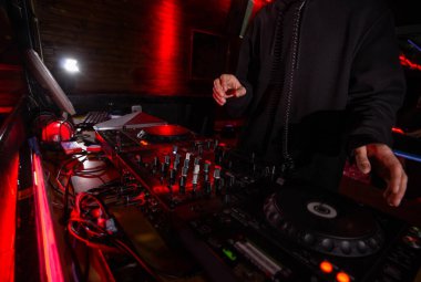 DJ eller ekipman güvertesinde ve mikser partisinde. Gece kulübünde siyah kapüşonlu diskjokeyin müziği karıştırdığı bir kare. Gece hayatı konsepti. Arkadaşlarıyla takılıyor..