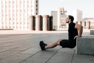 Taş küpten iten formda bir adam. Dışarıda sabah sporu. Siyah spor giyim. Kollarını güçlendirmek için sıkı çalışan bir adam. Şehir sporu konsepti. Sabah sporu. Arkaplanda şehir.