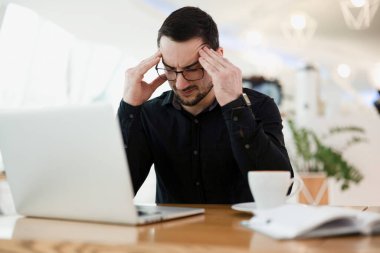 Çalışmıyor. Yorgun erkek programcı şakaklara masaj yapıyor, başını tutuyor ve kodda bir hata arıyor. Kafede kahve içen uzak ya da bağımsız bir işçi..