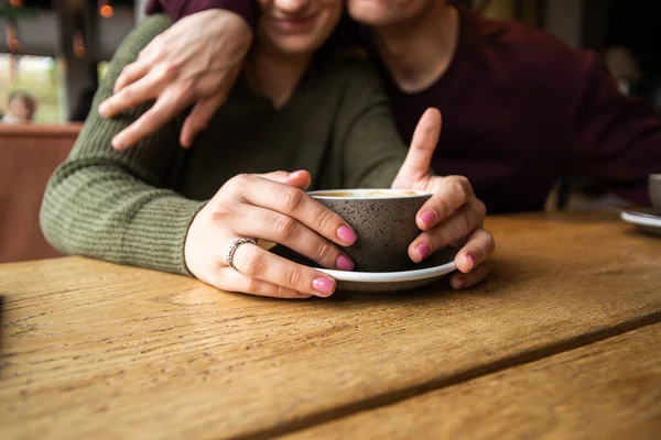 Casal jovem desfocado no café. Mulher segurando xícara de café quente quando o homem a abraça. Ambiente acolhedor no café. Xícara de cappuccino ou branco liso. Casal feliz abraçando no café. — Fotografia de Stock