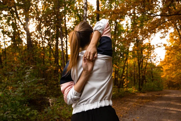 Een vrouw die oefeningen doet om achter haar rug om te vergrendelen. Aantrekkelijke jonge vrouw wandelen in park of bos. Zicht van achteren. Fit vrouw opwarmen en voor te bereiden op joggen. Park of bos op achtergrond. — Stockfoto