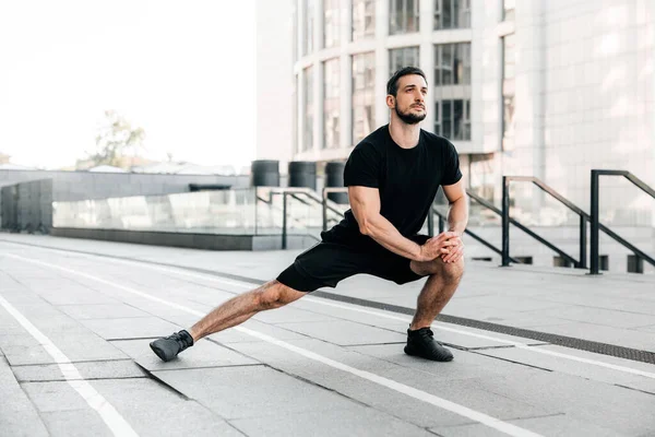 Koşucu yan hamleler yapıyor. Eğitimden önce esneme egzersizleri yapan sporcu portresi. Erkek sporcu dışarıda koşuya hazırlanıyor. Aktif spor yaşam tarzı konsepti. Tam uzunluk.