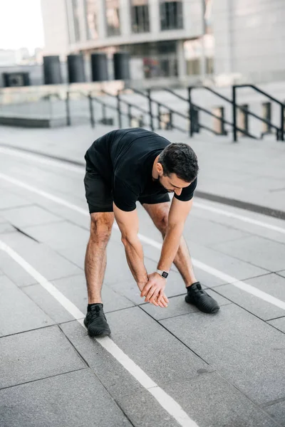 Fit man stretching back before jogging. Urban sport concept. Male runner stretches and warms up before jogging. Morning activity concept. Gray city on background.