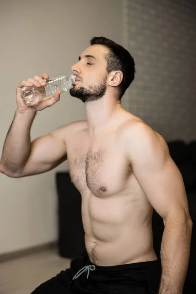 Hombre atractivo en topless beber agua después de un duro entrenamiento en casa. Tiempo de descanso. Deportivo hombre musculoso beber agua después de hacer ejercicio. Entrenamiento de culturismo. Concepto de hidratación y fitness. — Foto de Stock