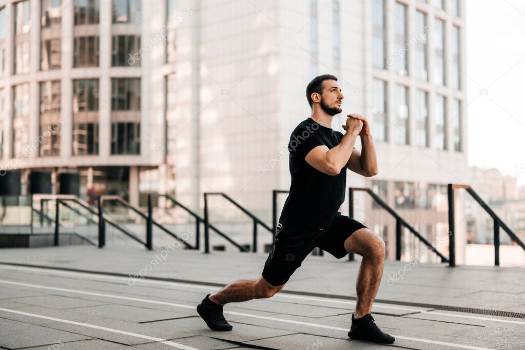 Fit man doing lunge forward. Sport in big city concept. Strong man stretching legs before jogging. Healthcare concept. Runner in black sportswear. Urban sport concept.