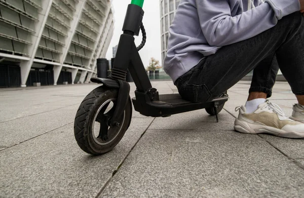 Guy resting after long trip around city on rented scooter. Cut close up view. Casual clothes. Man sitting or e-scoooter. Gray apartment bloacks on background. — Stock Photo, Image