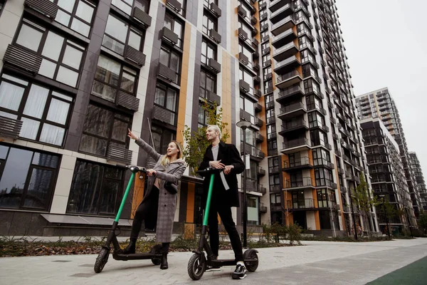 Laten we er naar toe gaan Vrouw die met haar hand laat zien waar ze wilde rijden op gehuurde e-scooters. Een man die naar haar luistert en lacht. Gelukkig stel. Elektrische scooters voor publiek gebruik. — Stockfoto