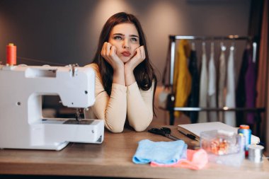 Genç terzi kadın dikiş makinesine elbise dikiyor. Atölyedeki bir terziyi hayal edip merak ediyordum. Çevrimiçi giyim tasarım kursları oluşturuluyor.