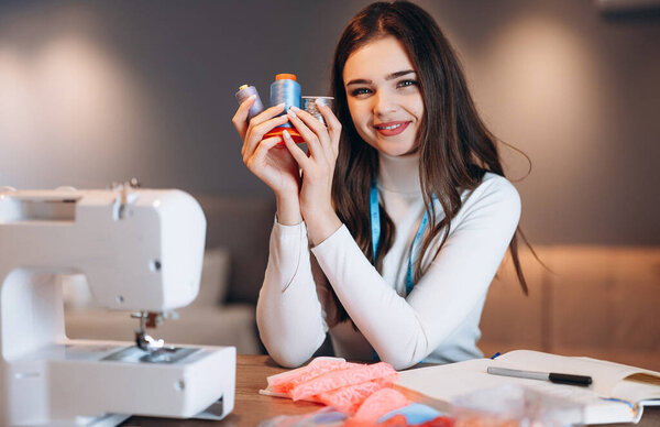 Молодая портниха шьет одежду на швейной машинке. Держать вязание в мастерской. Создание онлайн курсов по дизайну одежды.