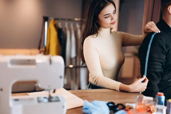 Mujer joven modista con máquina de coser. Las medidas de costura para el hombre en el taller. Creación de cursos de diseño de ropa en línea. — Foto de Stock