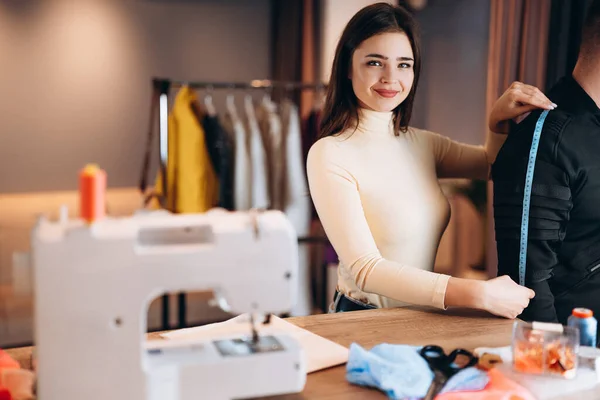 Mujer joven modista con máquina de coser. La costurera es la medida para el hombre en el taller. Creación de cursos de diseño de ropa en línea. — Foto de Stock